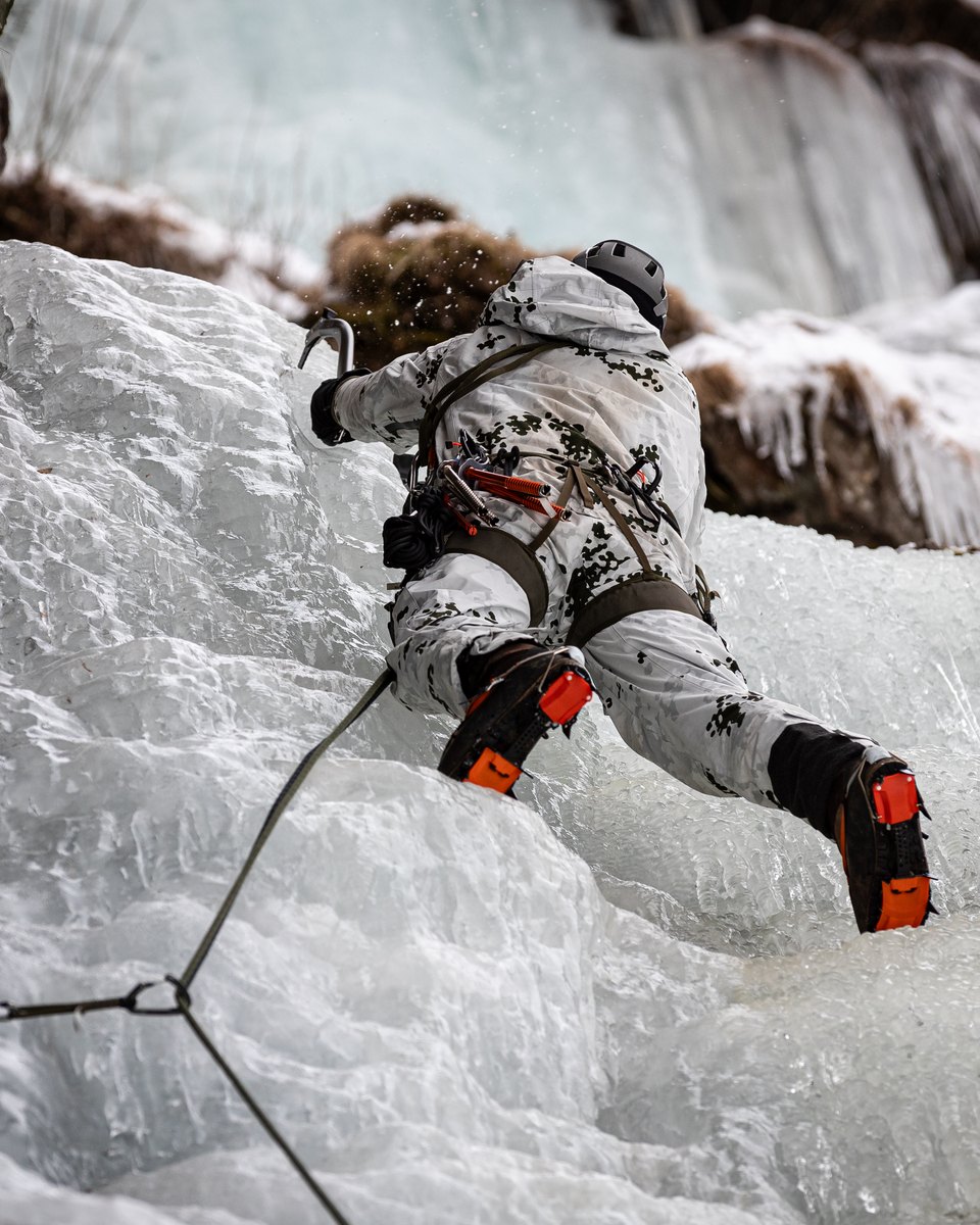 Kletterer in Schneetarn mit Helm und Steigeisen mit orangen Teilen im Eisfall