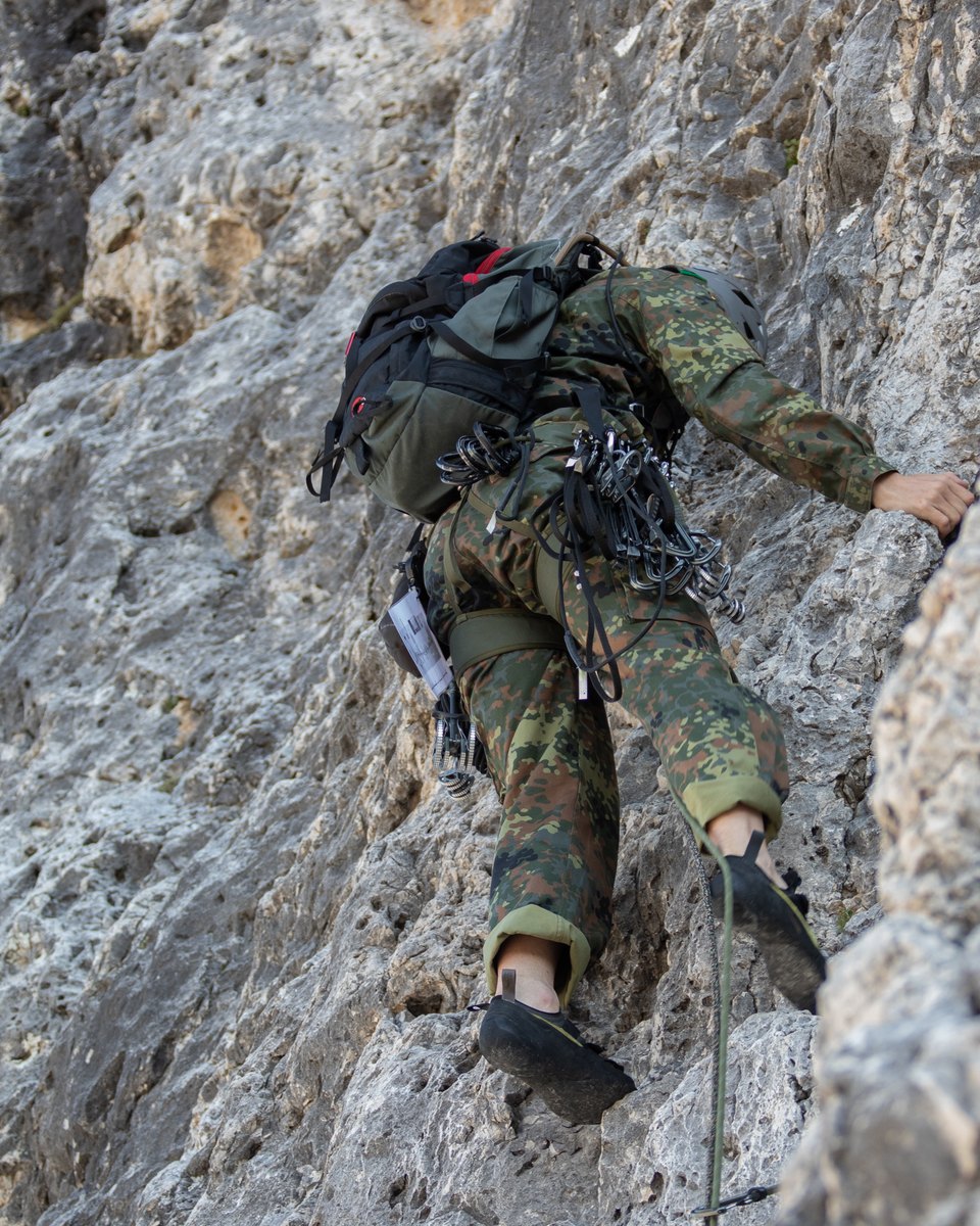 Soldat in Flecktarn mit Rucksack klettert am hellen Fels, von hinten gesehen