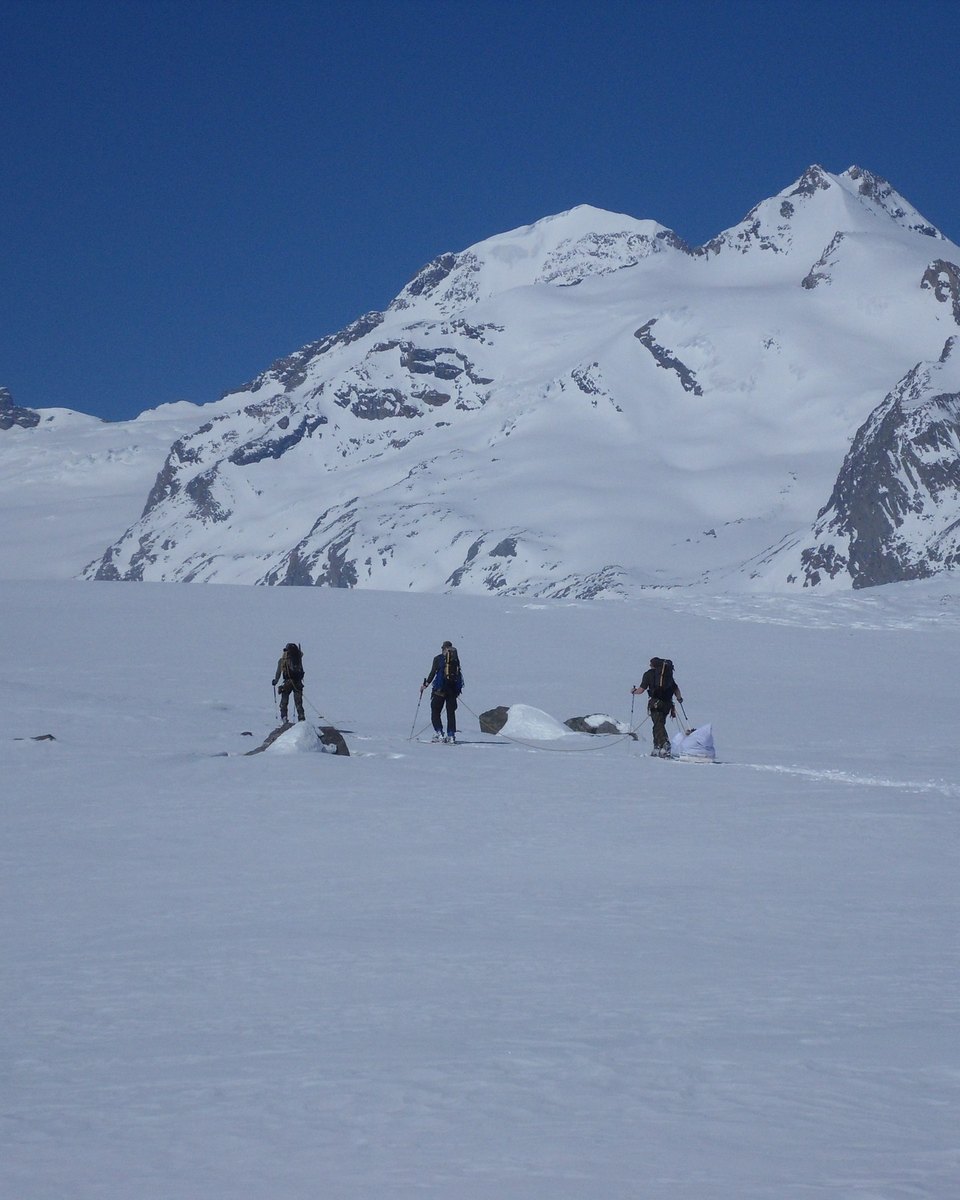 Drei Skitourengeher mit Pulka auf einem weiten Gletscher