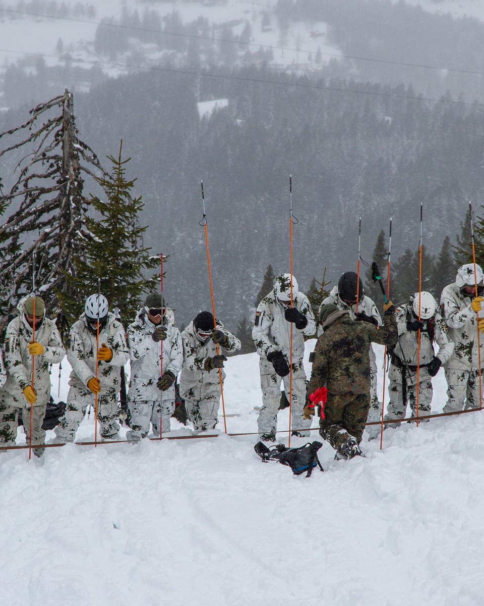 Soldaten in Schneetarn stehen nebeneinander und sondieren mit Lawinensonden den Schnee