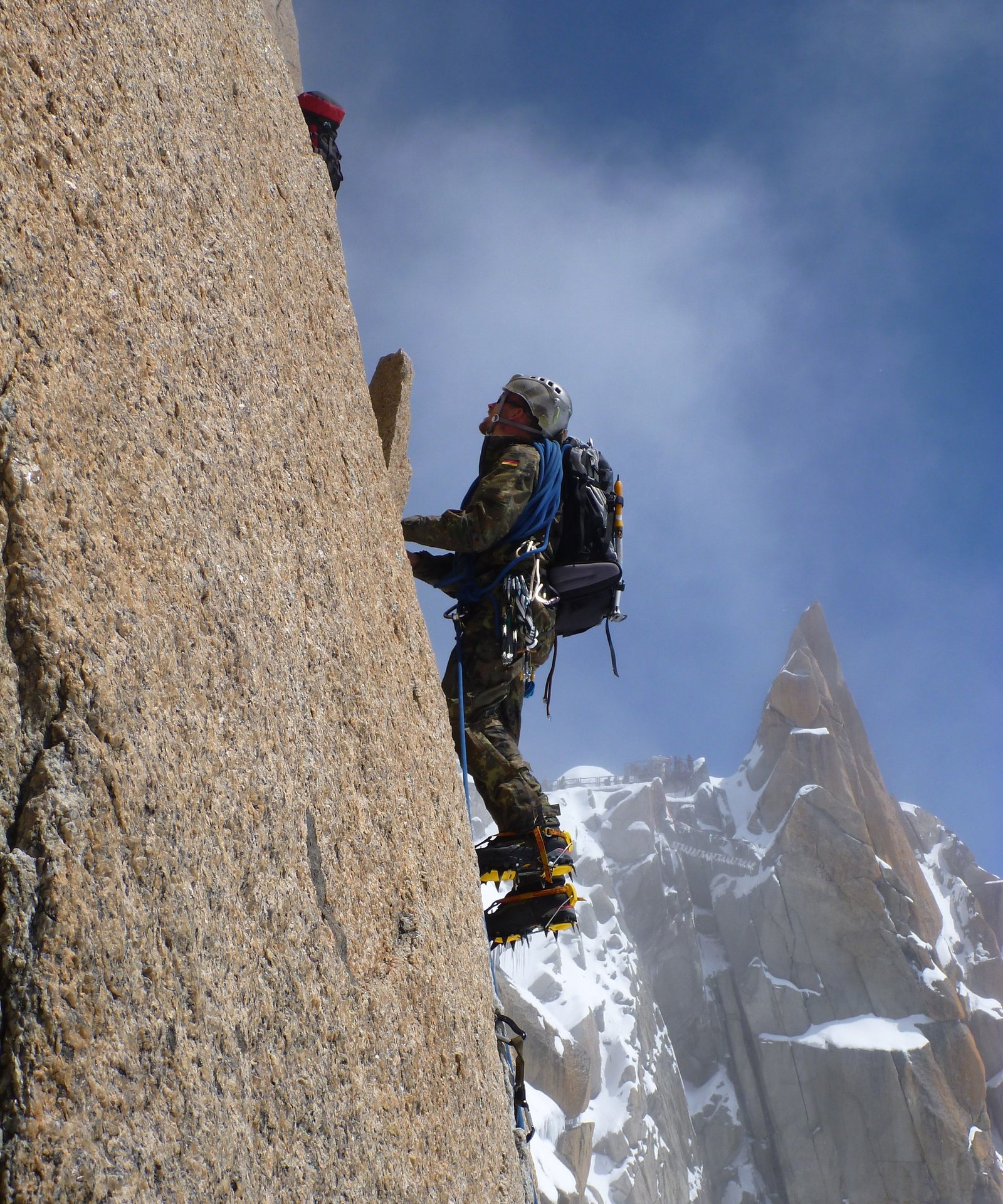 Soldat mit Helm und Steigeisen klettert eine Granitplatte hinauf, dahinter spitze Felsnadeln
