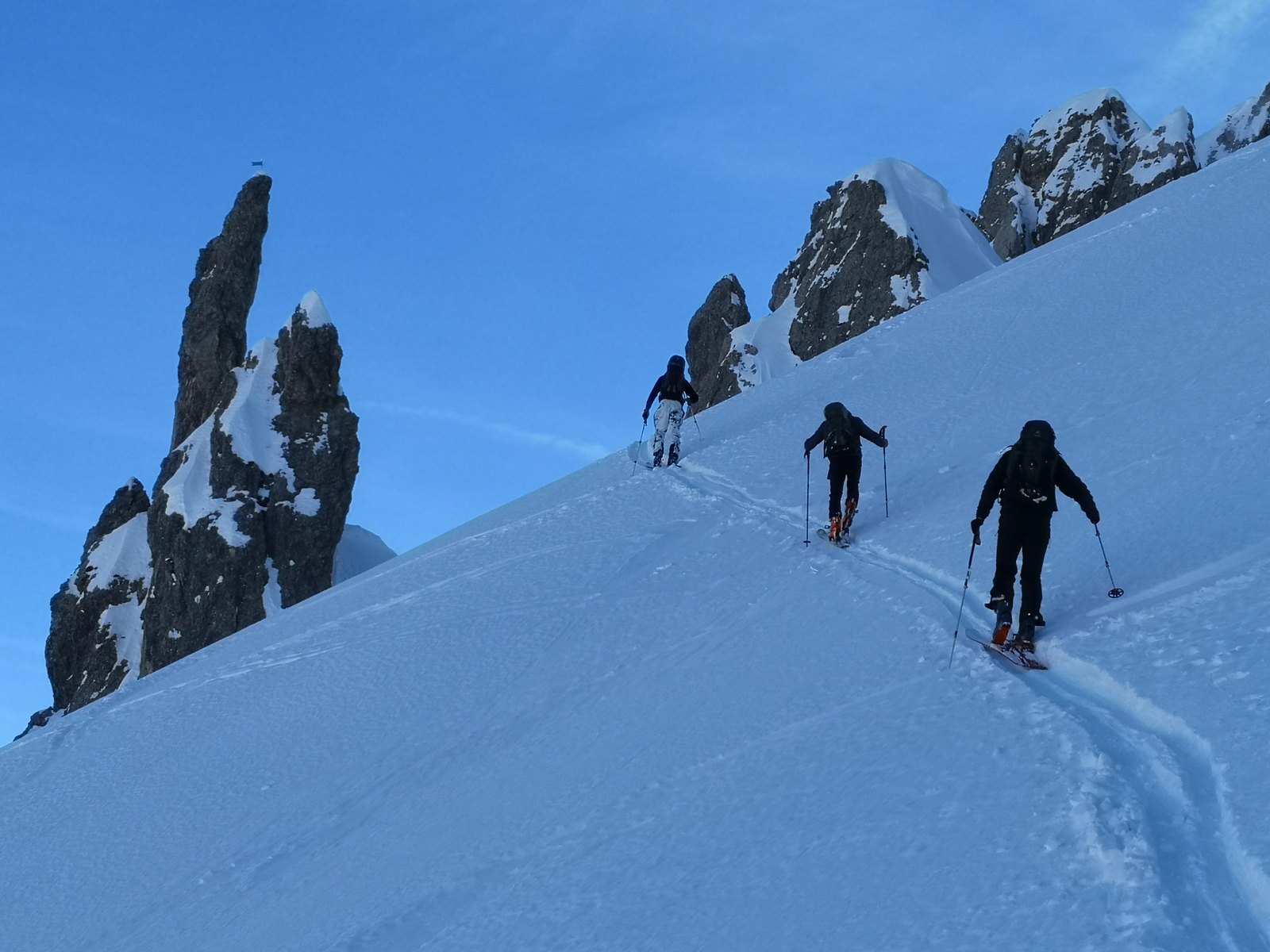 Drei Skitourengeher steigen unter Felsnadeln einen Hang hinauf