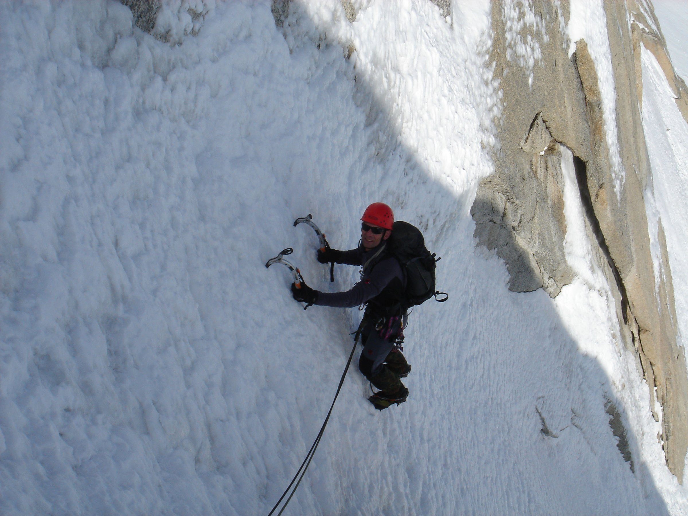 Ein Bergsteiger mit rotem Helm klettert mit zwei Eisgeräten im Steileis