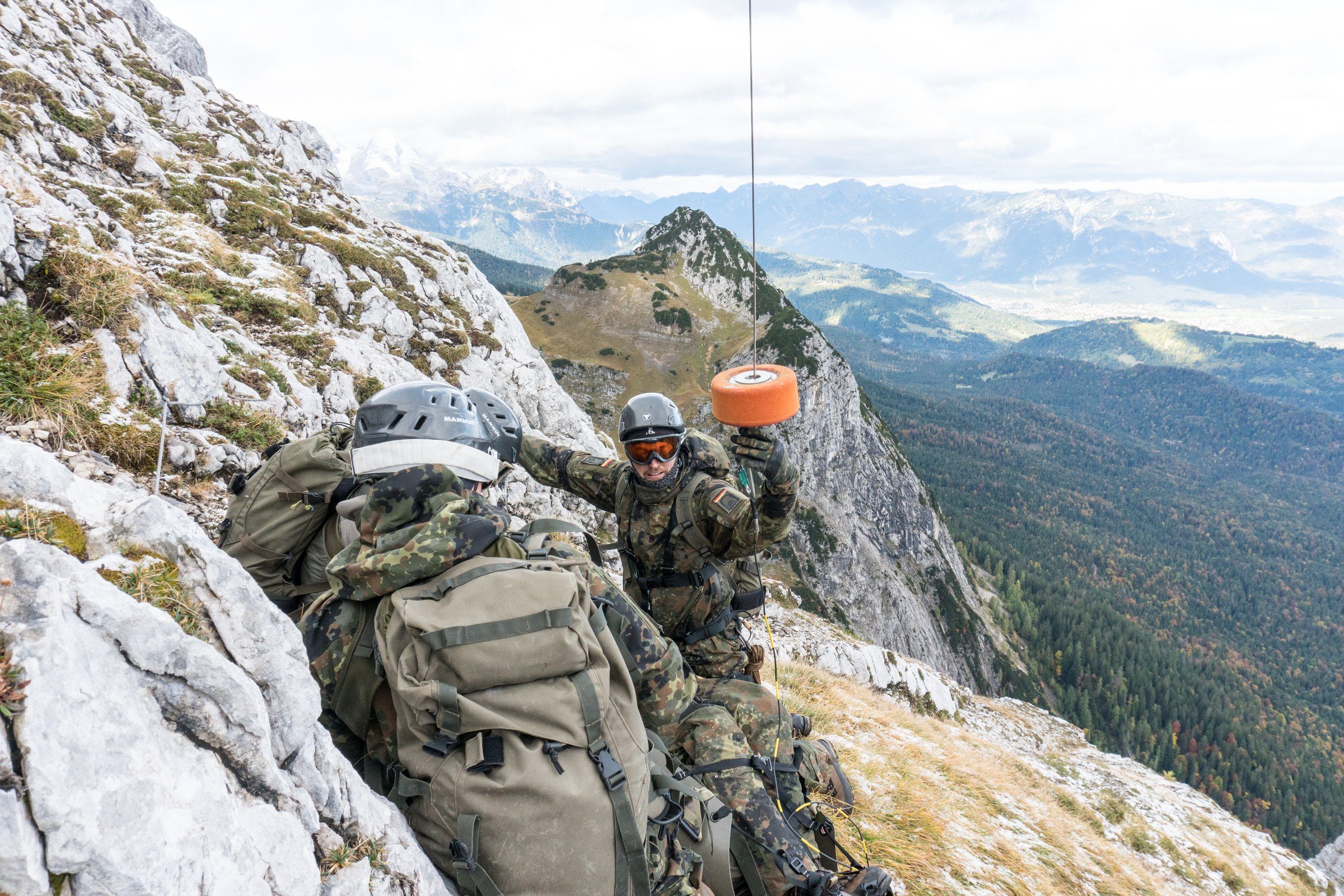 Soldaten an einem Felshang nehmen den Haken einer Hubschrauberwinde an
