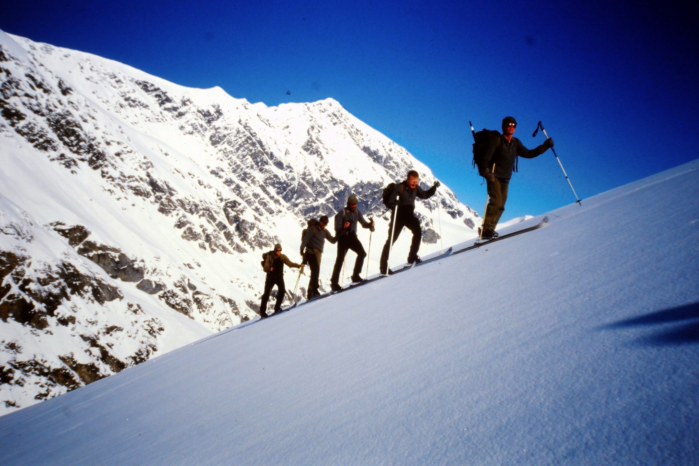 Fünf Skibergsteiger steigen in einer Reihe einen steilen Schneehang hinauf