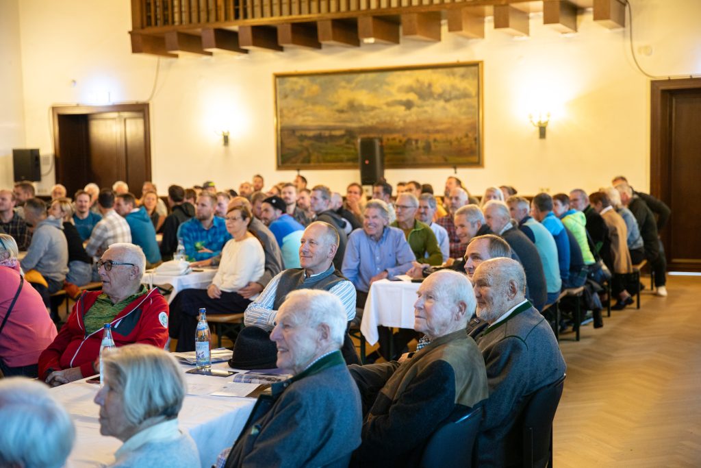 Festakt: Gäste an Tischen im Festsaal, dahinter ein großes Gemälde