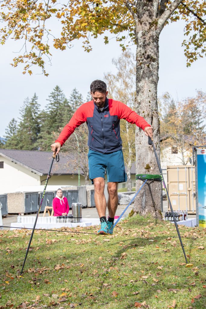 HBF-Olympiade: Mann balanciert mit Stöcken auf einer Slackline im Freien