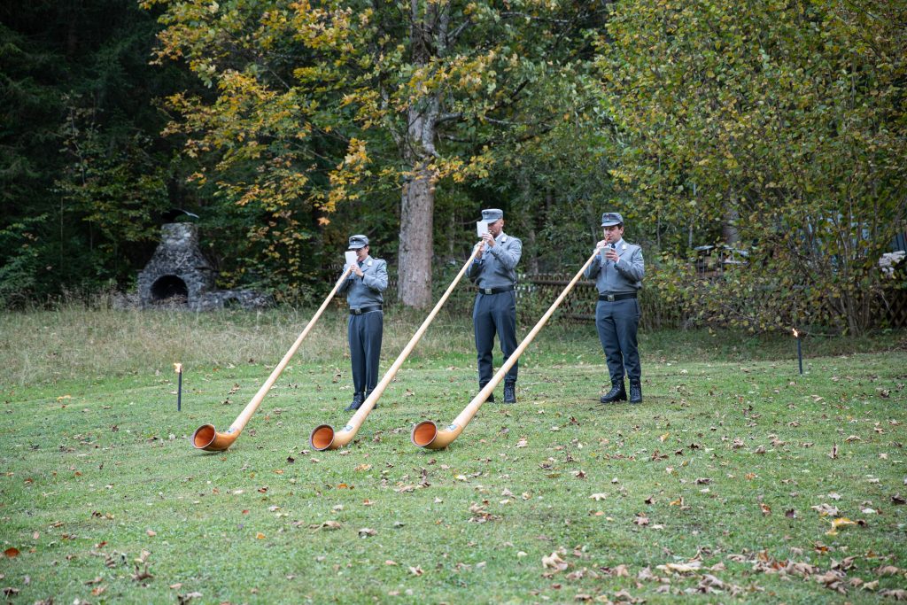 Alphornblasen: Drei Alphornbläser in Uniform spielen auf der Wiese