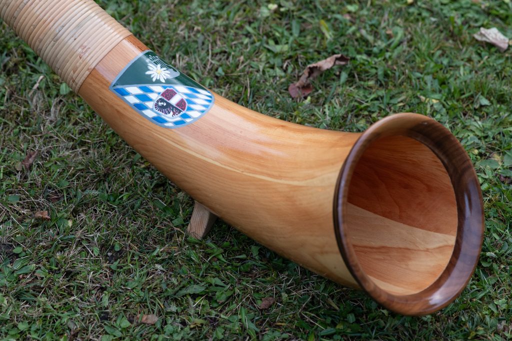 Alphornblasen: Nahaufnahme eines Alphorns mit Wappen am Schalltrichter im Gras