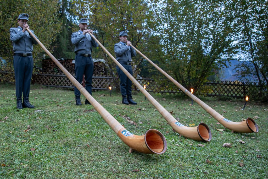 Alphornblasen: Alphornbläser in der Dämmerung, zwischen den Hörnern brennen Fackeln