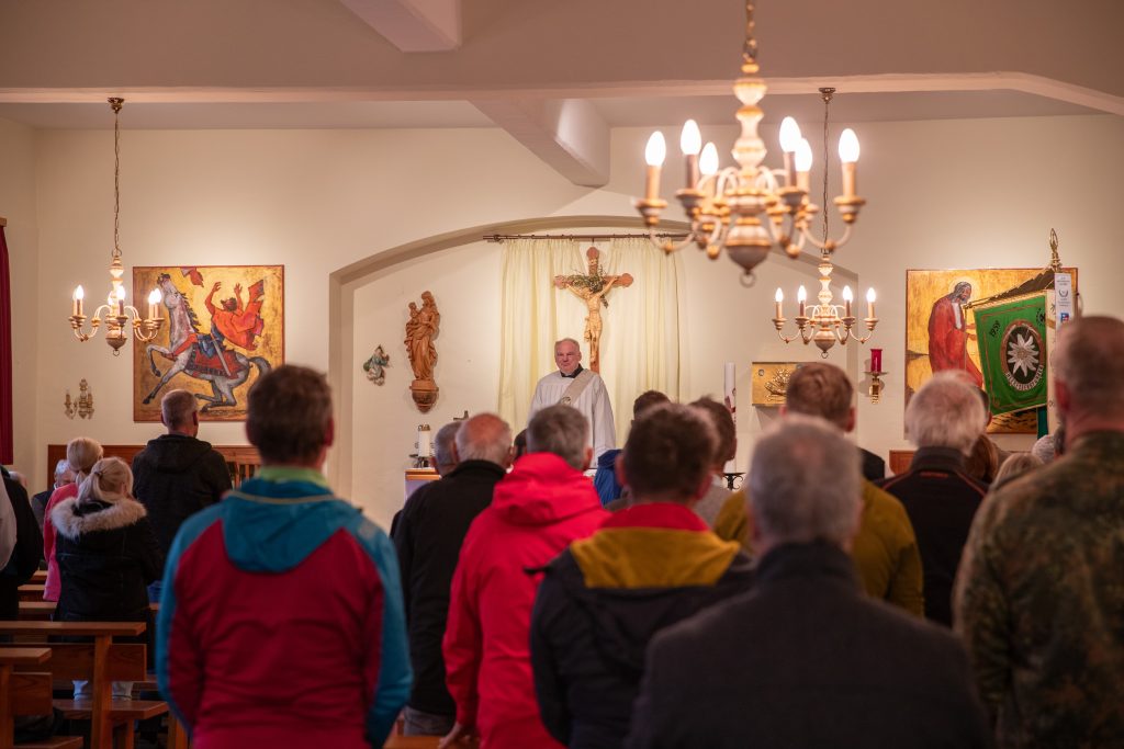 Gottesdienst: Gemeinde steht in der Kapelle, vorn der Geistliche am Altar