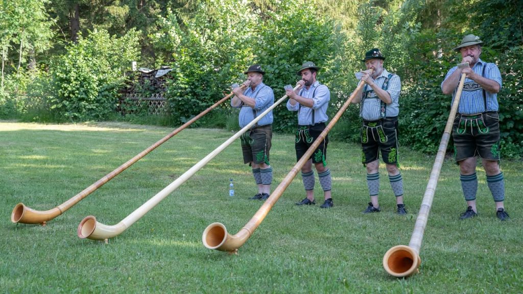 Vier Alphornbläser in Tracht spielen auf einer Wiese