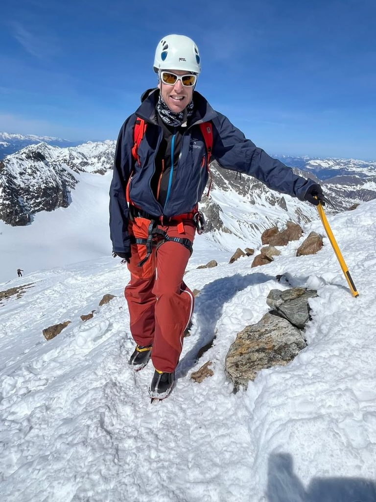 Bergsteiger mit Helm, Gurt und Eispickel auf verschneitem Gipfelgrat