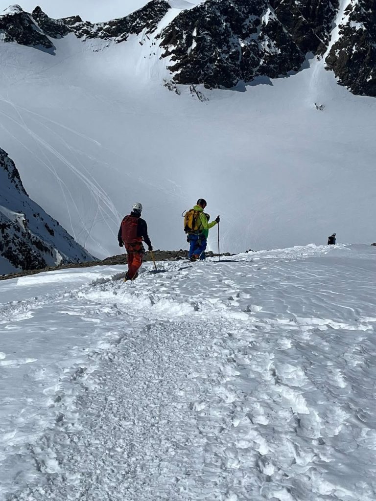 Zwei Bergsteiger steigen über einen verschneiten Grat, darunter ein weites Gletscherbecken