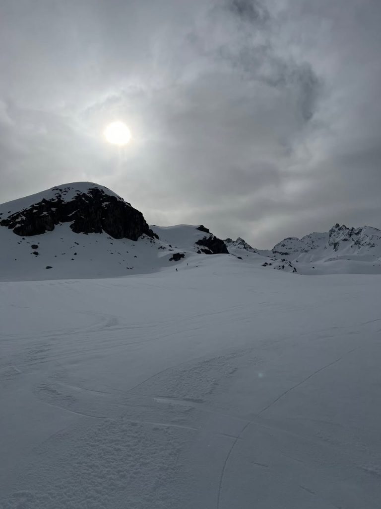 Verschneite Berglandschaft mit Felskuppe und diffuser Sonne hinter Wolken