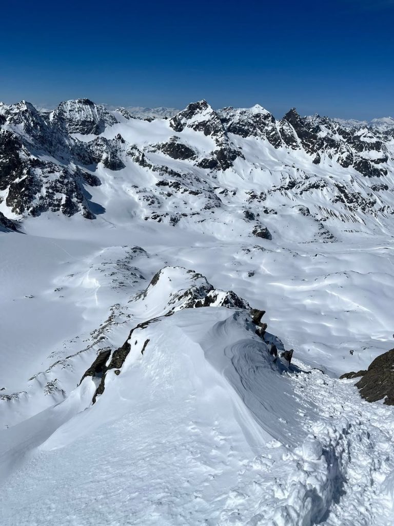 Blick vom Gipfel über verschneite Grate und Gletscher unter tiefblauem Himmel