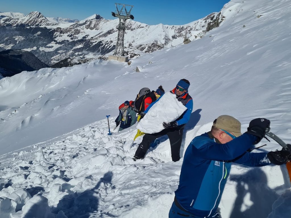 Lawinenfortbildung: Teilnehmer graben im Hang, einer trägt einen großen Schneeblock