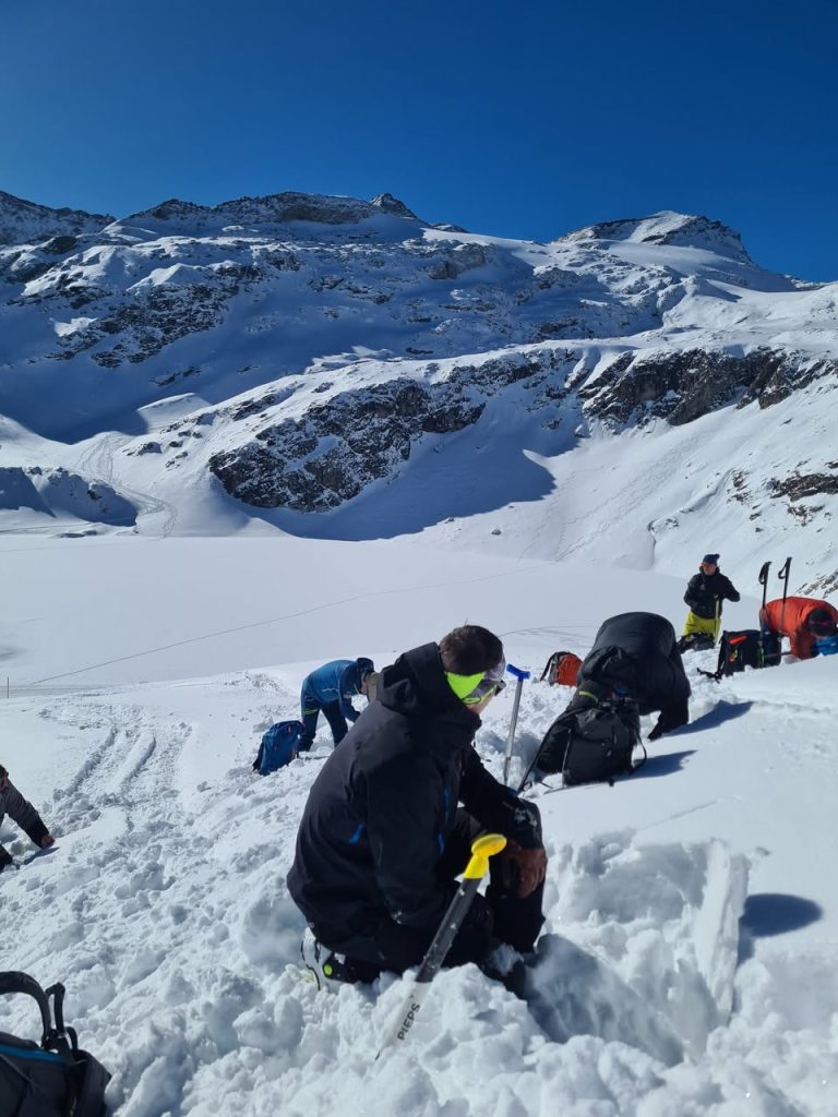 Teilnehmer graben Schneeprofile, im Vordergrund eine Lawinenschaufel